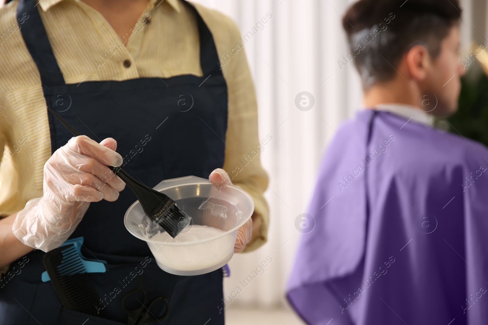 Photo of Professional hairdresser holding bowl with hair dye in beauty salon, closeup