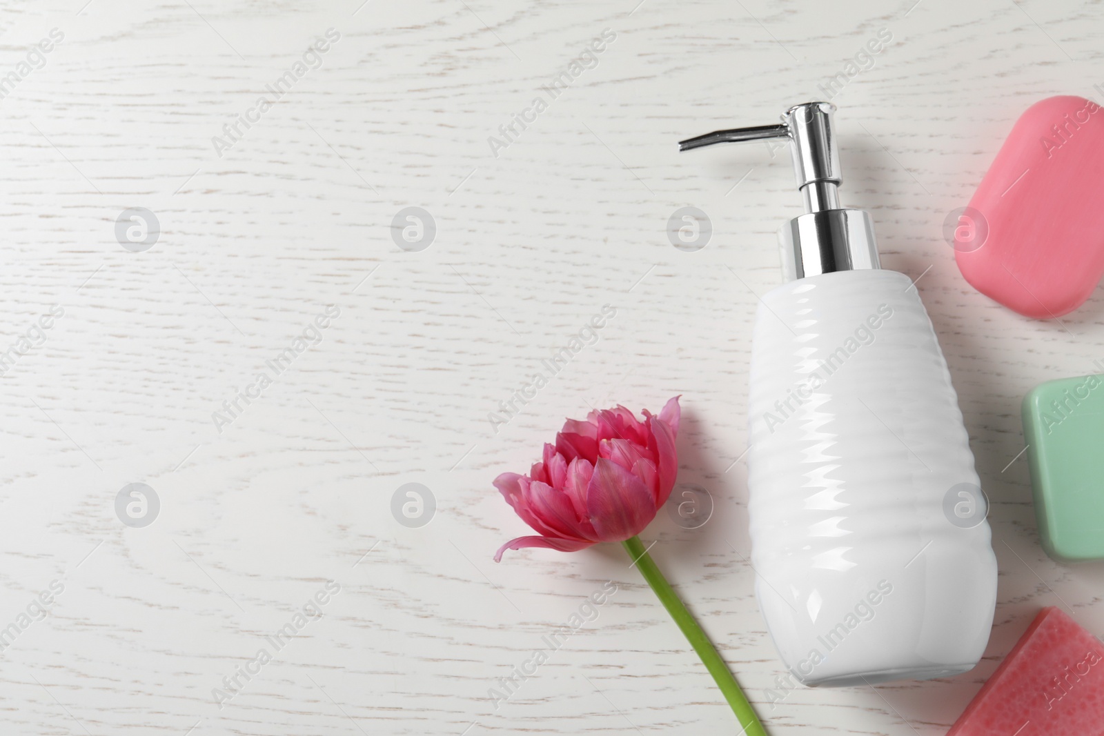 Photo of Soap bars, dispenser and tulip on white wooden table, flat lay. Space for text