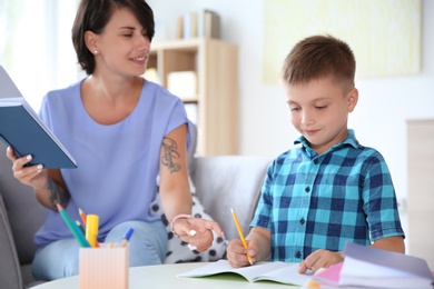 Photo of Young woman helping her child with homework at home. Elementary school