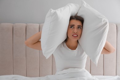 Photo of Unhappy young woman covering ears with pillows in bed at home. Noisy neighbours