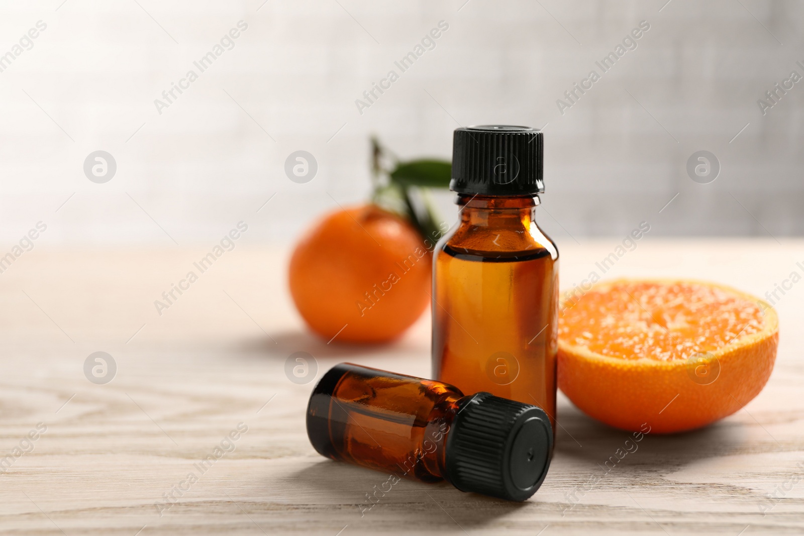 Photo of Bottles of tangerine essential oil and fresh fruits on wooden table, closeup. Space for text