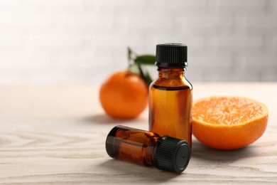 Bottles of tangerine essential oil and fresh fruits on wooden table, closeup. Space for text