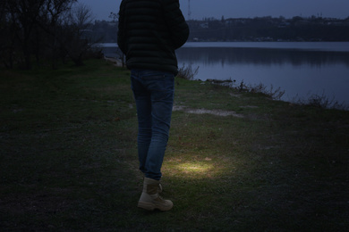 Photo of Man with flashlight walking near river, closeup