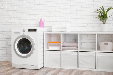 Modern washing machine near brick wall in laundry room interior