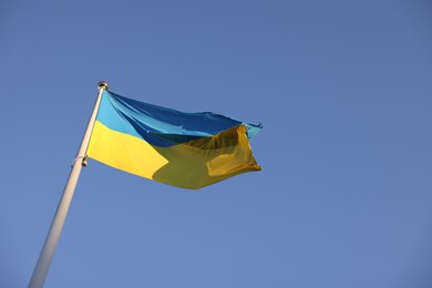 Flag of Ukraine fluttering against blue sky, low angle view. Space for text