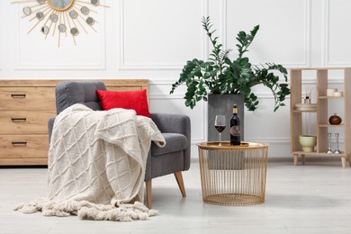 Stylish living room interior with comfortable armchair, blanket, side table and houseplant
