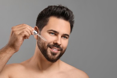 Photo of Handsome man applying cosmetic serum onto face on grey background, space for text