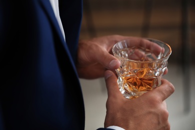 Young man with glass of whiskey indoors, closeup view