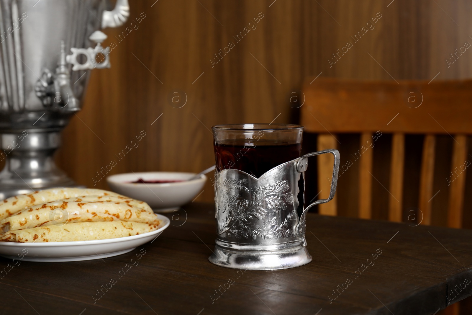 Photo of Vintage samovar, cup of hot drink and pancakes served on wooden table. Traditional Russian tea ceremony