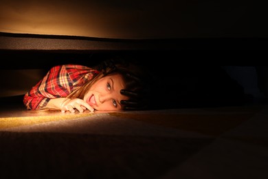 Photo of Childhood phobia. Little girl with monster under bed at home, closeup