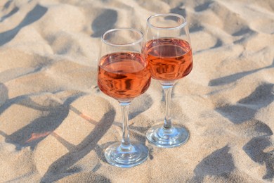 Photo of Glasses of tasty rose wine on sand