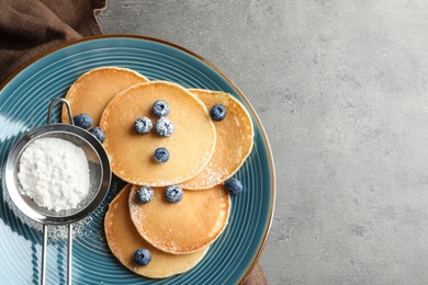 Photo of Plate with pancakes, berries and sugar powder on grey background, top view