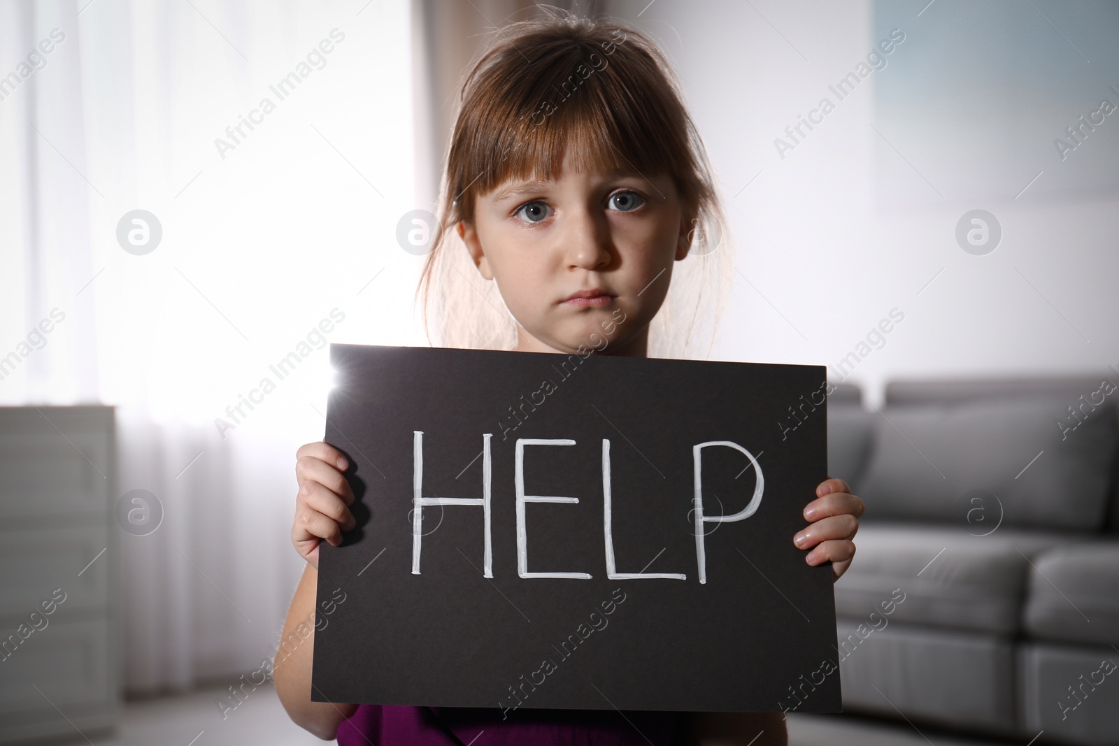 Photo of Abused little girl with sign HELP indoors. Domestic violence concept