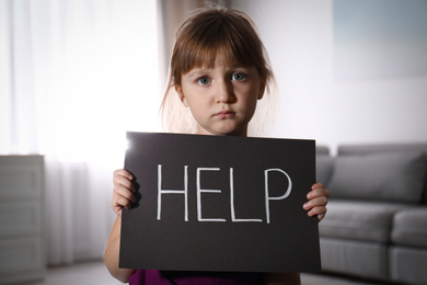 Abused little girl with sign HELP indoors. Domestic violence concept