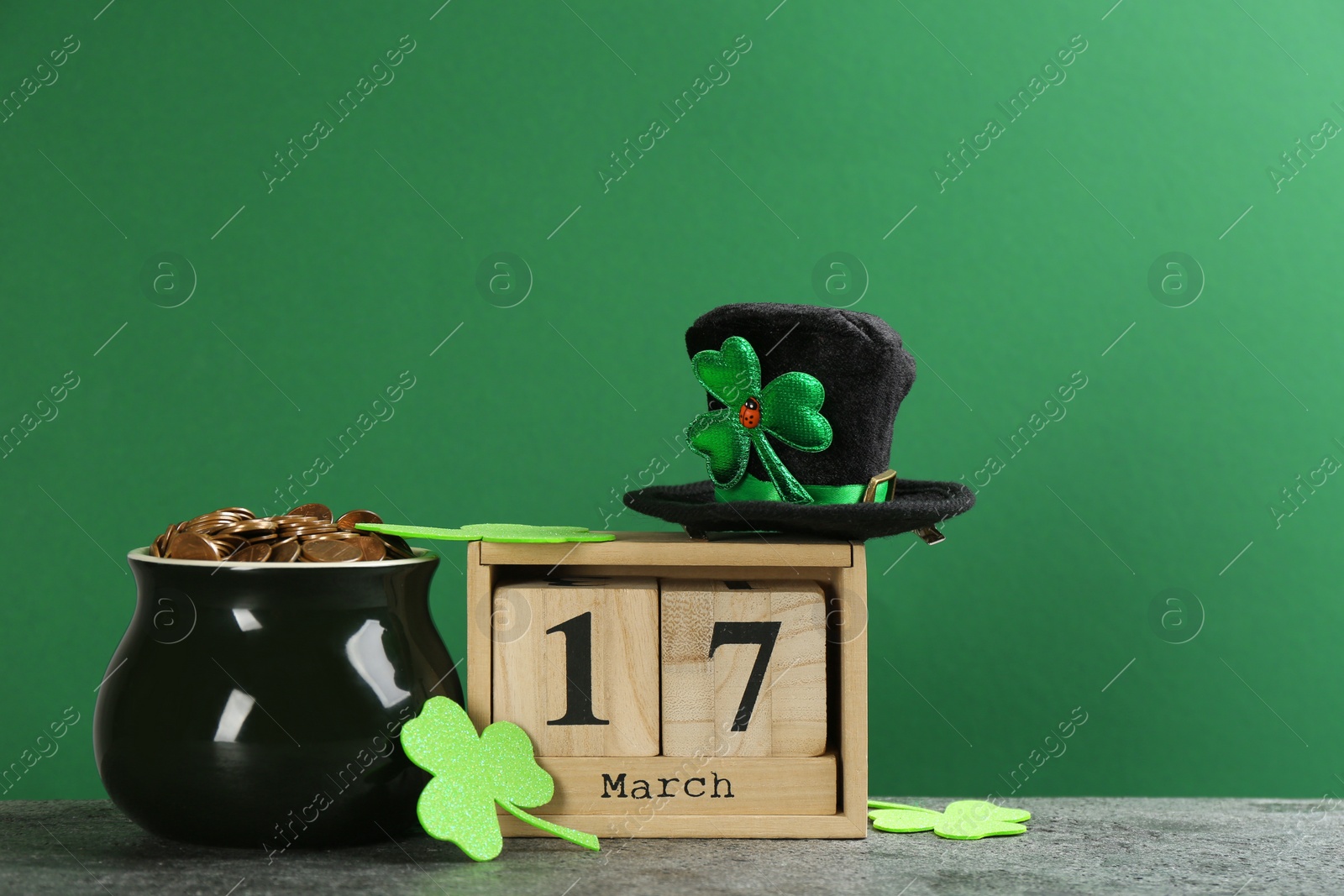 Photo of Composition pot of gold coins and wooden block calendar on grey stone table against green background. St. Patrick's Day celebration