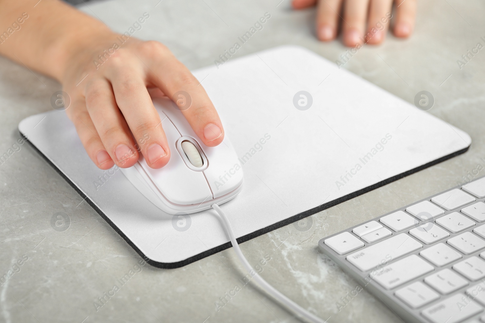 Photo of Woman using wired computer mouse on pad at light grey marble table, closeup