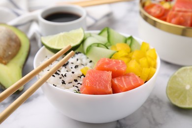 Delicious poke bowl with salmon, lime and vegetables on white marble table, closeup