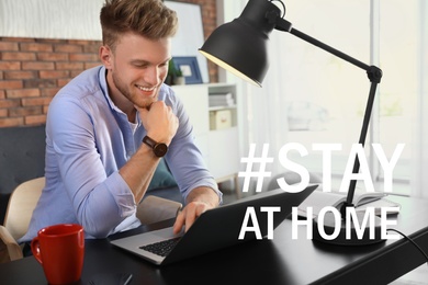 Hashtag Stay At Home - protective measure during coronavirus pandemic. Young man working with laptop at table indoors