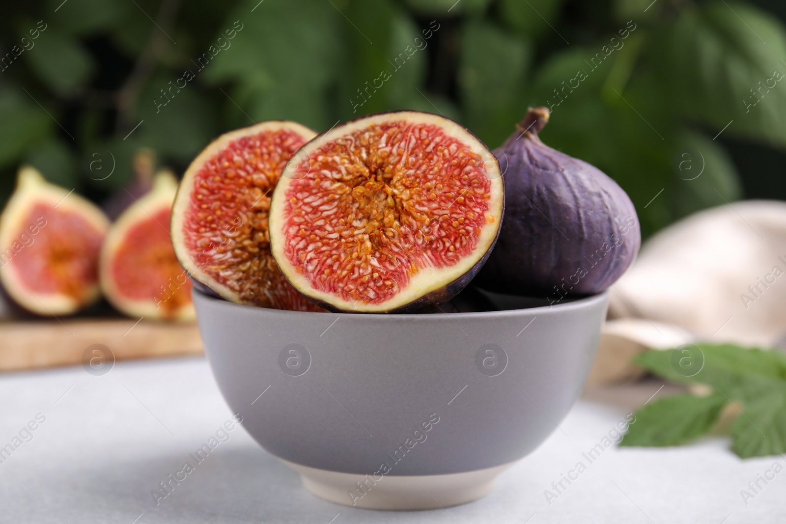 Photo of Bowl of tasty ripe figs on light table against blurred background, closeup