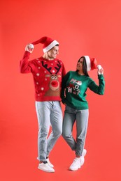 Photo of Beautiful happy couple in Santa hats and Christmas sweaters on red background