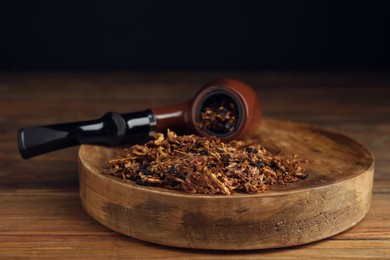 Photo of Board with smoking pipe and dry tobacco on wooden table against dark background