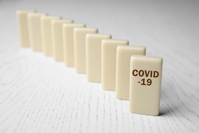 Photo of Domino tiles on white wooden table, closeup. Spreading of coronavirus concept