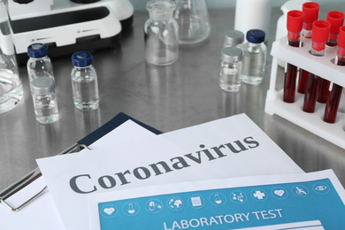 Clipboard with laboratory test list and word CORONAVIRUS on grey table, closeup