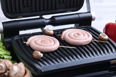 Photo of Homemade sausages and mushrooms on electric grill, closeup