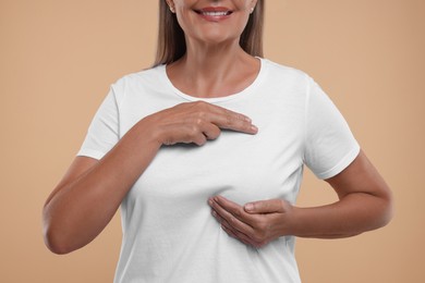 Photo of Woman doing breast self-examination on light brown background, closeup