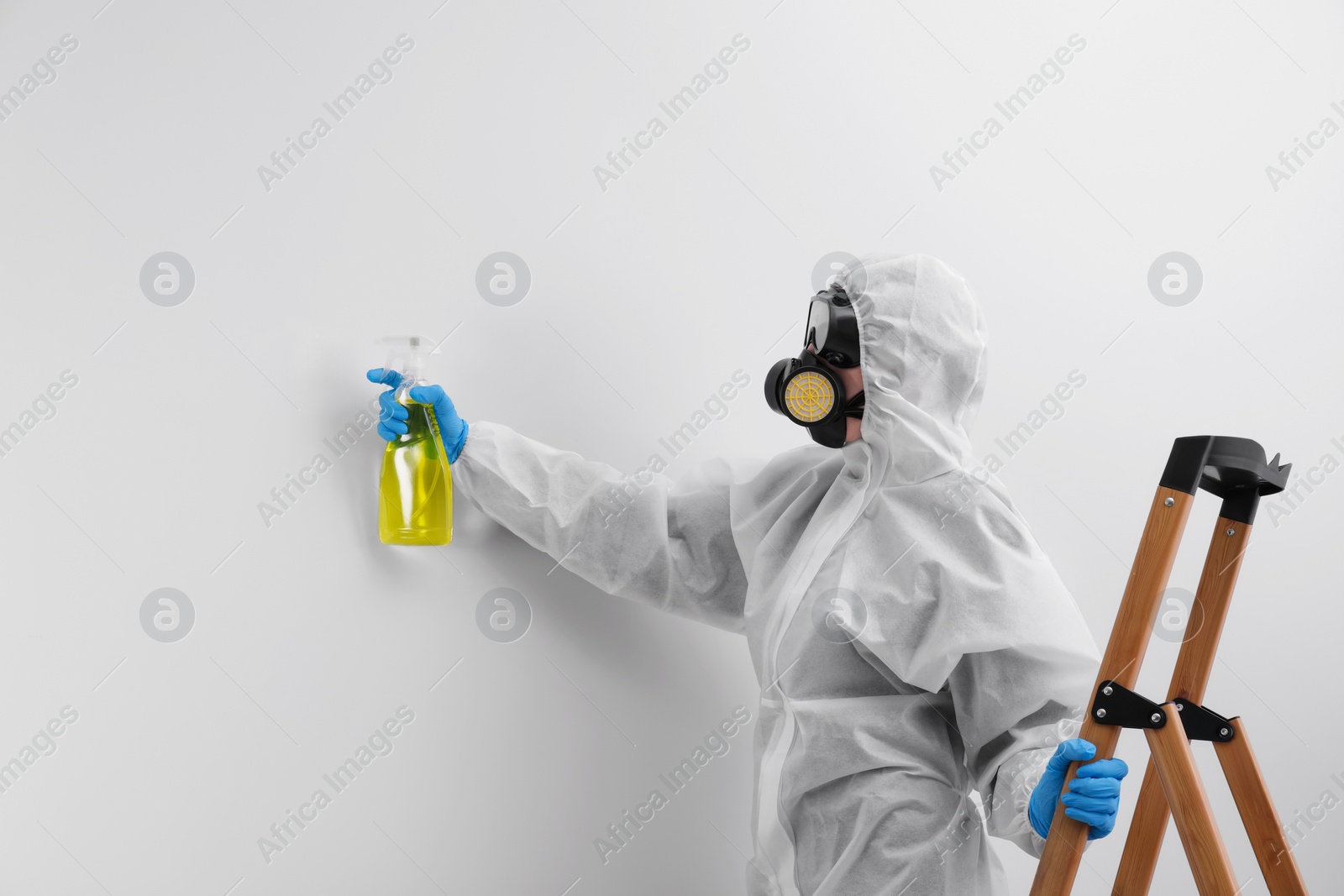 Photo of Woman in protective suit cleaning mold with sprayer on wall
