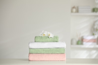 Photo of Stack of clean soft towels with orchids on white table indoors