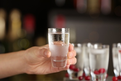 Photo of Woman holding shot of vodka on blurred background, closeup