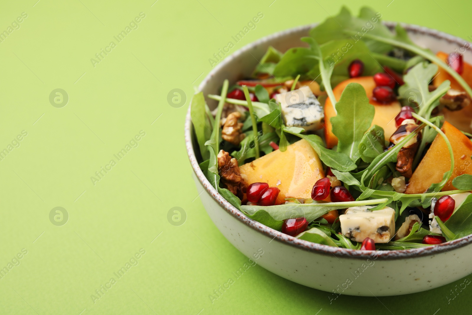 Photo of Tasty salad with persimmon, blue cheese, pomegranate and walnuts served on light green background, closeup. Space for text