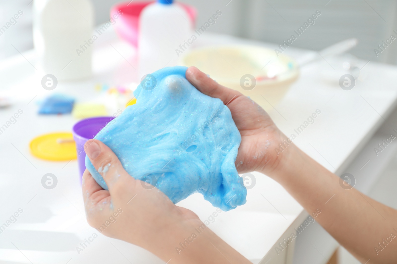 Photo of Little girl making DIY slime toy at table, closeup