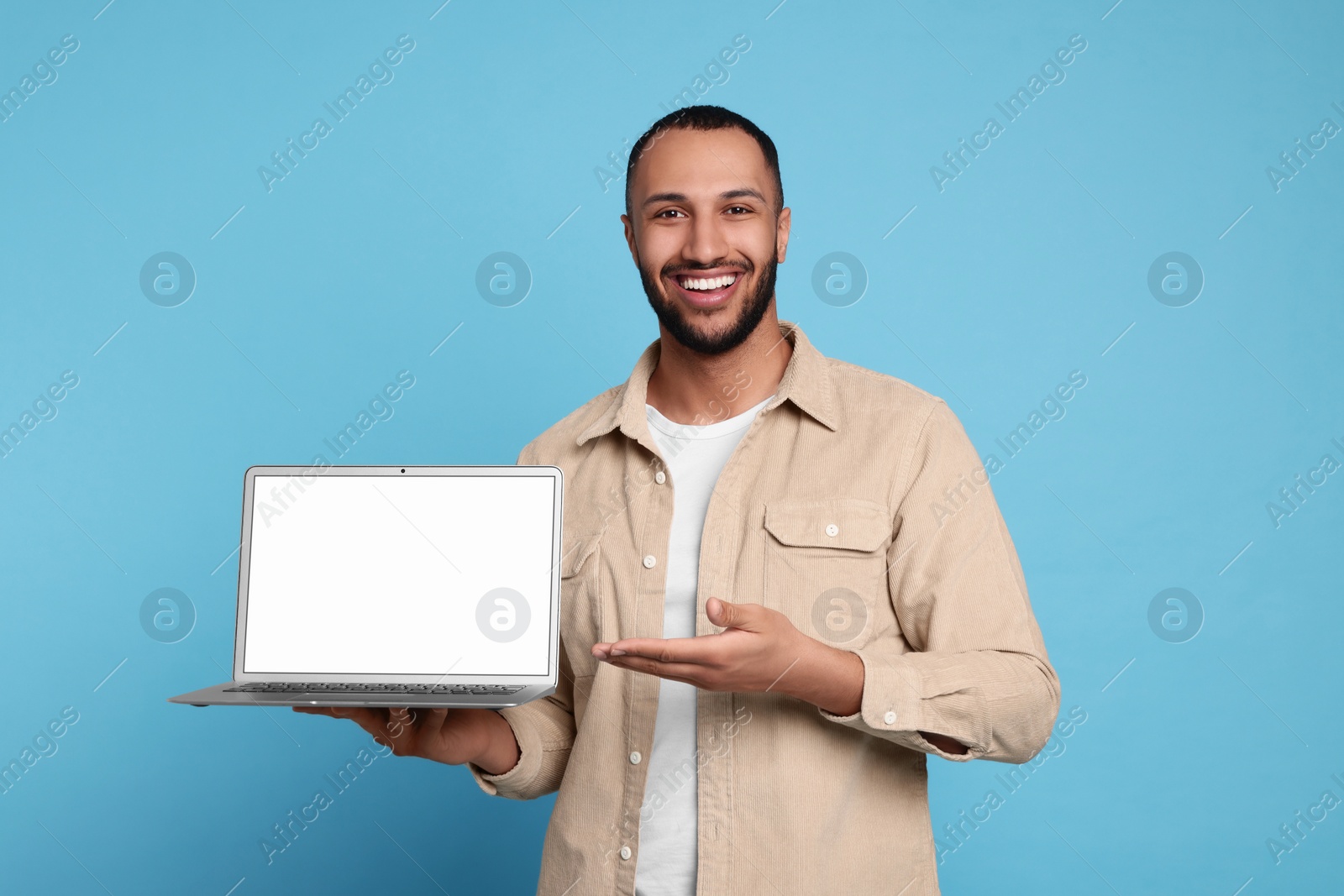 Photo of Smiling young man showing laptop on light blue background