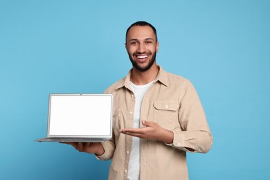 Photo of Smiling young man showing laptop on light blue background