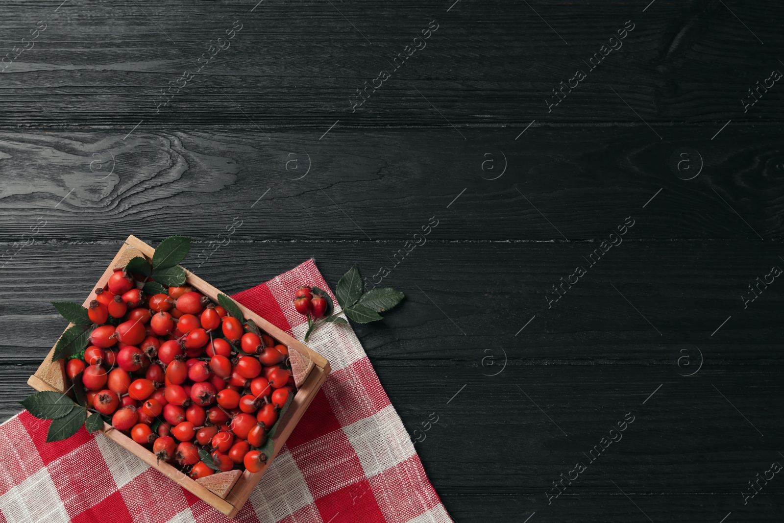 Photo of Ripe rose hip berries with green leaves on black wooden table, flat lay. Space for text