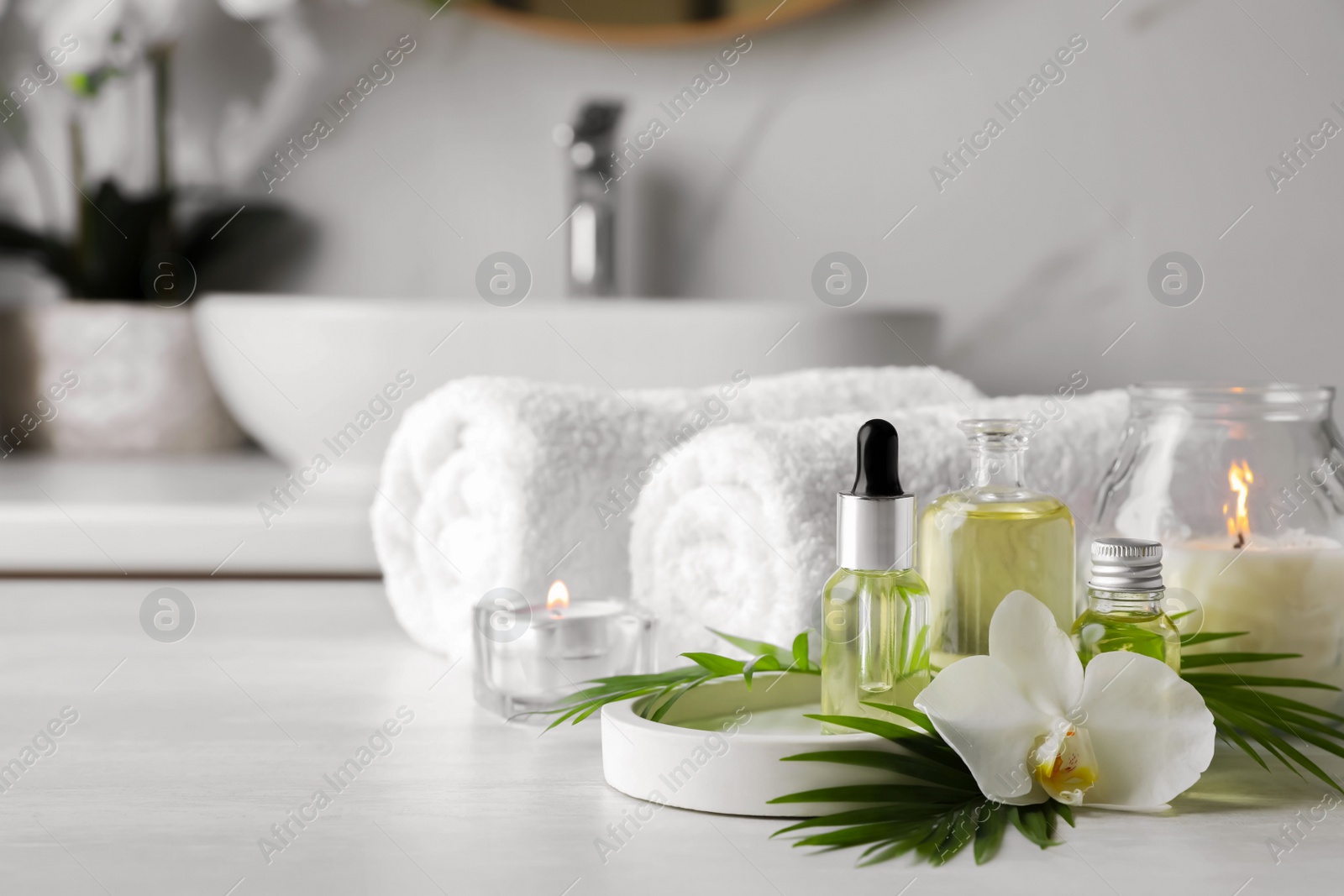 Photo of Essential oils, orchid flower and towels on white countertop in bathroom. Space for text