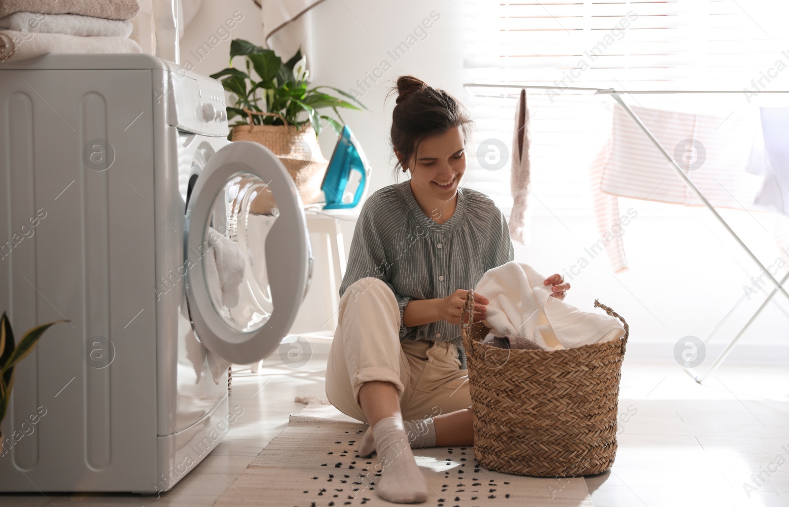 Photo of Young woman with laundry basket near washing machine at home