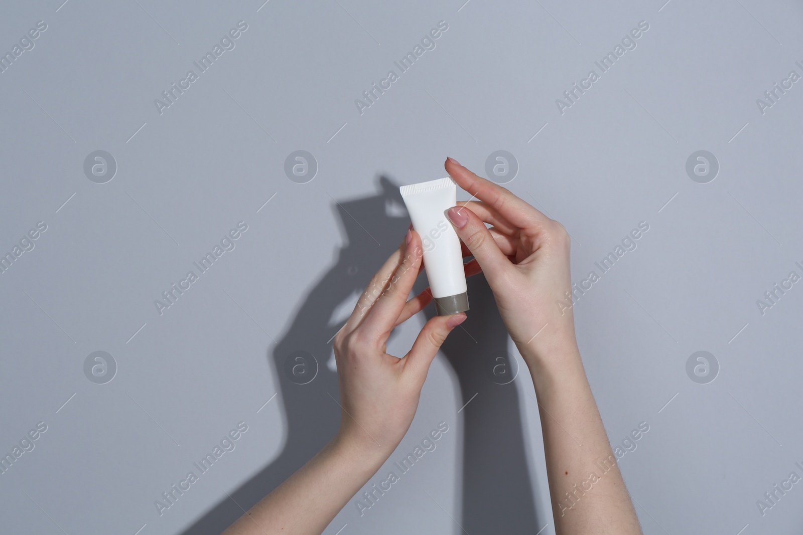 Photo of Woman holding tube of cream on grey background, closeup