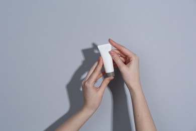 Woman holding tube of cream on grey background, closeup