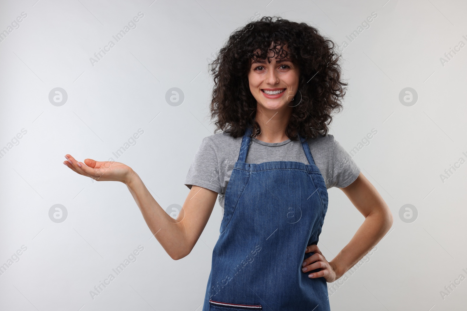 Photo of Happy woman wearing kitchen apron on light grey background. Mockup for design