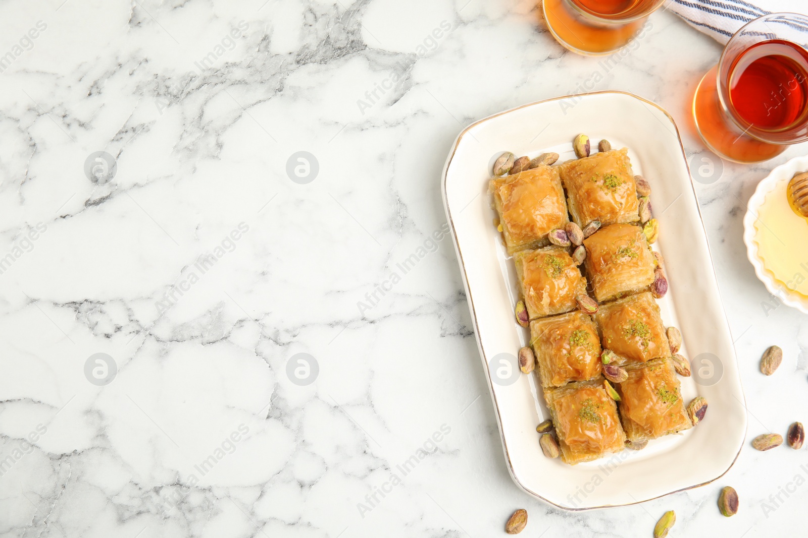 Photo of Delicious baklava with pistachios, nuts and hot tea on white marble table, flat lay. Space for text