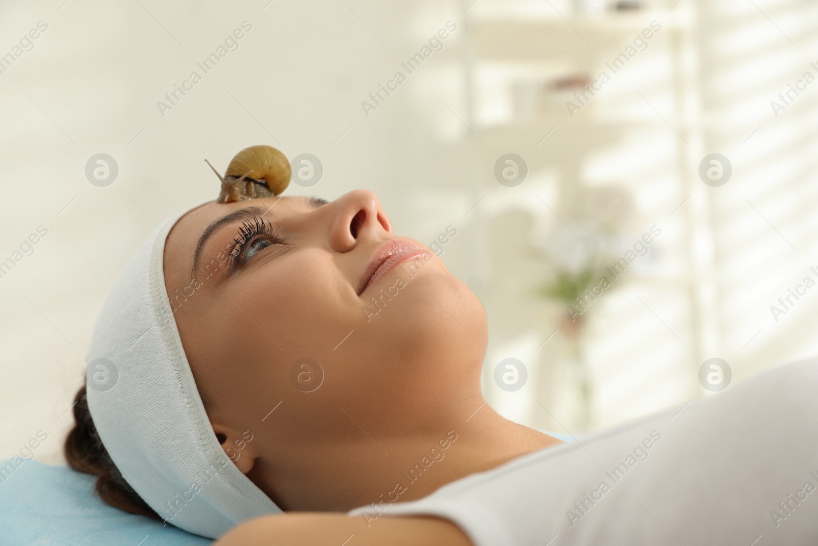 Photo of Young woman receiving snail facial massage in spa salon