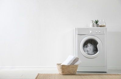 Photo of Modern washing machine and laundry basket near white wall indoors, space for text. Bathroom interior