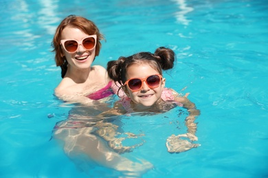 Photo of Young woman teaching her daughter to swim in pool
