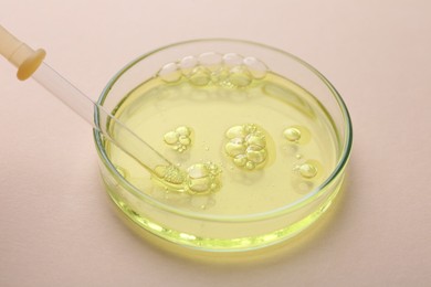 Photo of Petri dish with color liquid sample and pipette on beige background, closeup