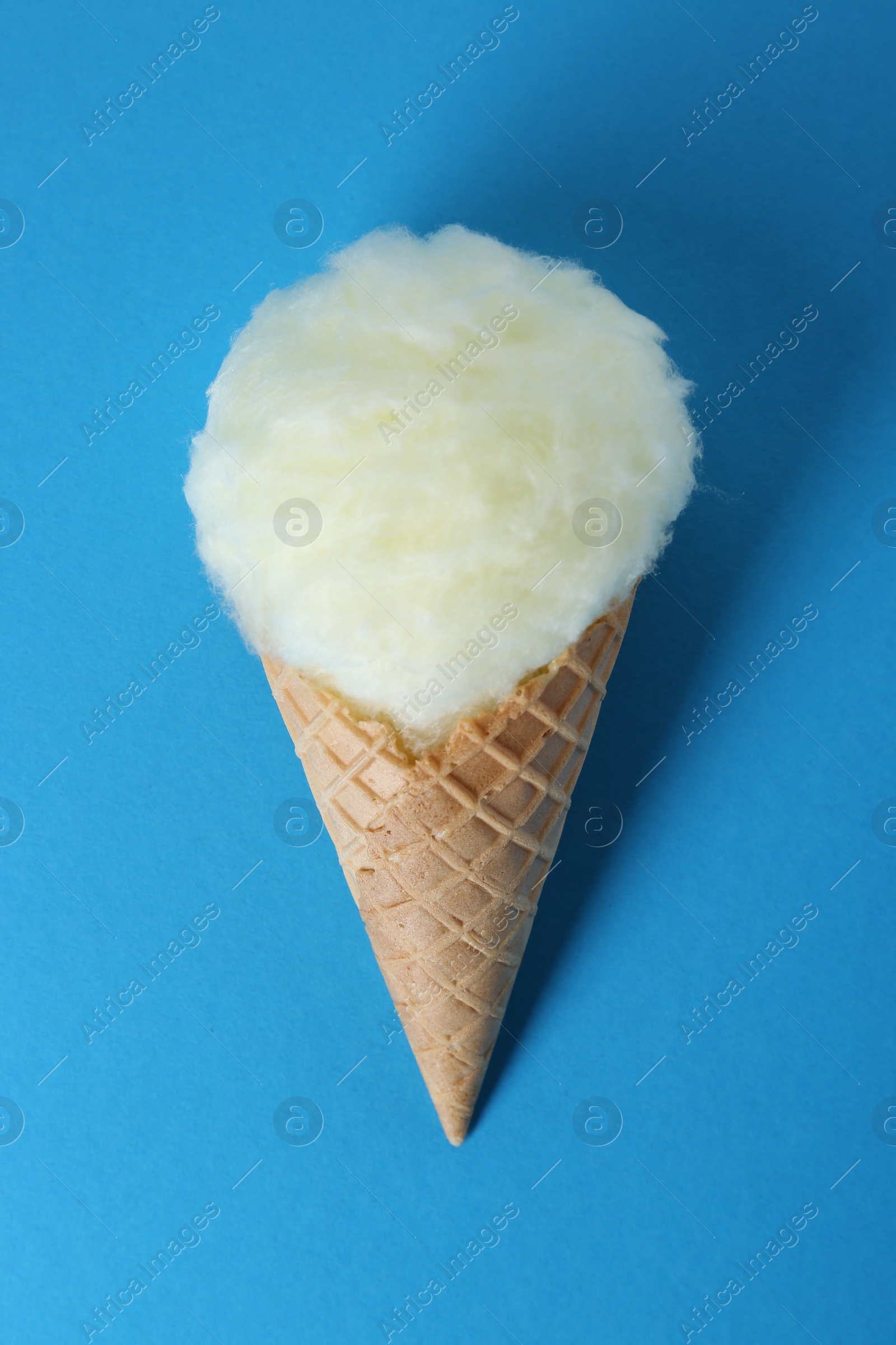 Photo of Sweet cotton candy in waffle cone on blue background, top view