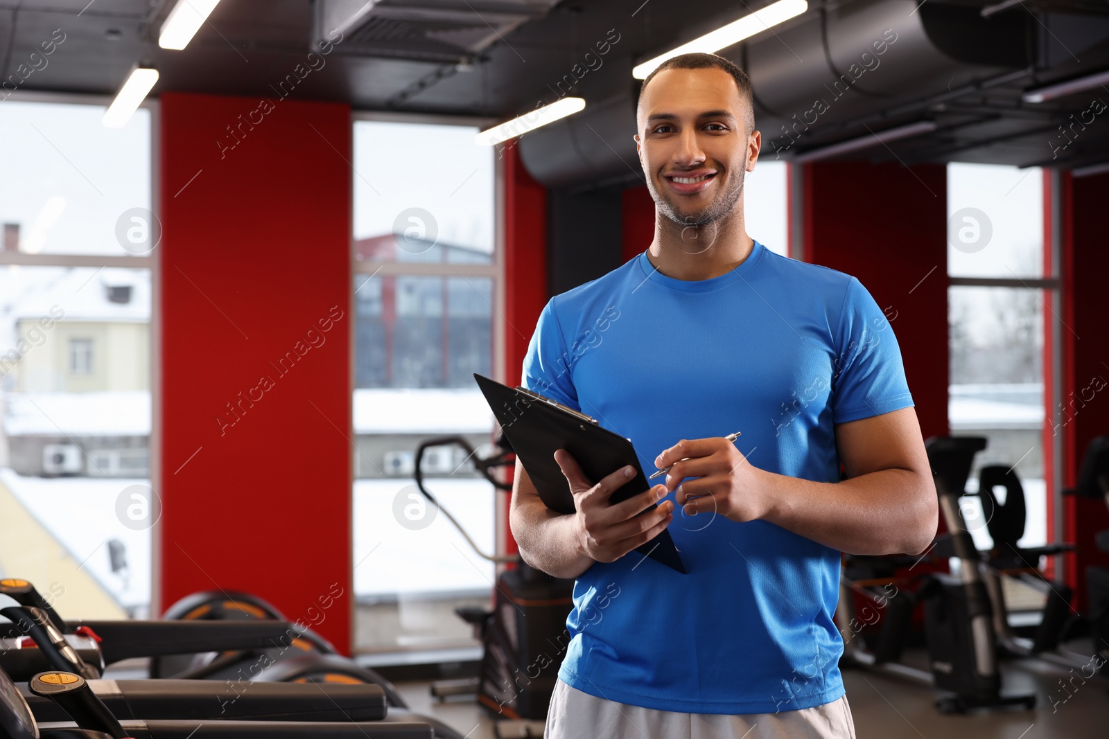 Photo of Happy trainer writing down workout plan in modern gym, space for text