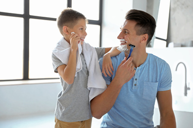 Son wiping face with towel while his dad shaving in bathroom